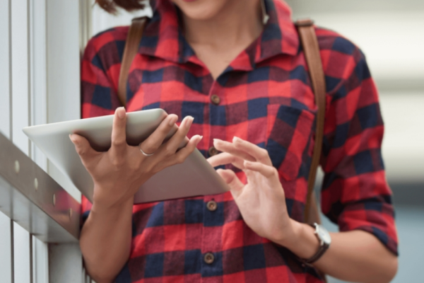 Mulher de camisa xadrez encostada em uma janela, lendo um tablet